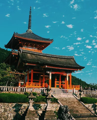 A building with a roof and steps stands in front of a hill