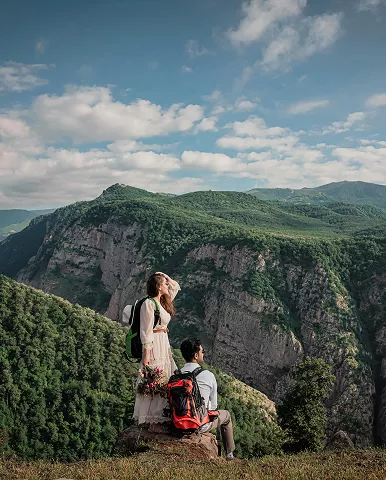 A couple sits on a rock, gazing at a scenic valley below