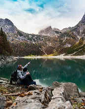 A couple sits on rocks by a serene lake