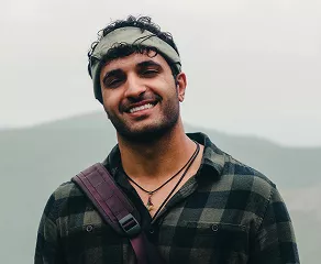 A man wearing a hat and a backpack stands outdoors