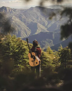A person stands in the mountains, holding a guitar