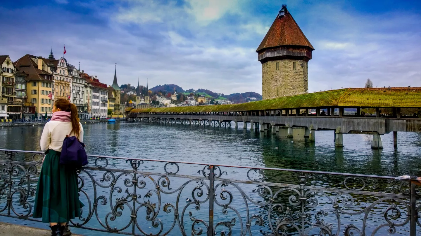 A woman stands on a bridge, gazing at a river and a town in the distance