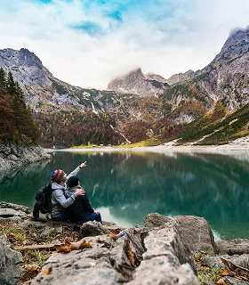 Two people sit on rocks by a serene mountain lake